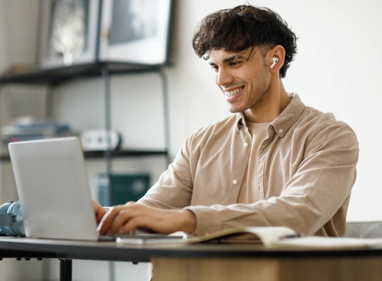 Persona con auriculares mirando su laptop mientras sonrie